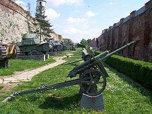 a small green-painted wheeled artillery piece with a split trail mounted on a concrete plinth