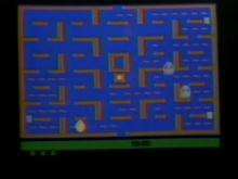 A video depicting the game's method of play. The main character travels through the corridors of a brown maze to eat white wafers, while avoiding four flickering ghosts.