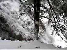  A video taken in winter from the trail starts by looking up to the head of the waterfalls and then pans slowly down and to the right to follow the falling water cascading down a stone face. The thundering water flows freely, but the surrounding rocks and trees are covered in snow and ice.