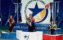 Three women stand holding flowers over their heads on a medal stands