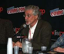 Denis Kitchen, a bespectacled middle-aged man, seated at a Comic Con dais