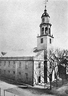 A black and white image of a church similar in plan to the one pictured elsewhere in the article, seen from slightly above at a three-quarter angle to its right. It has normal windows along the side and bare trees in front