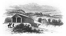 A black and white engraved image of a wooden covered bridge crossing a river with a two-story house in the background