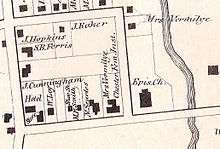 An old map showing a block of streets with lot lines and solid black rectangles representing buildings with their owners' names next to them. There is a river at the right