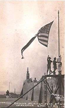 photograph of a walled fort with three Marines raising an American flag over it