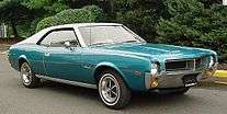 Shows a 1969 AMC Javelin finished in blue with optional white vinyl covered roof and Magnum 500 wheels
