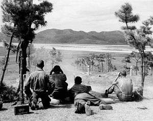 A machine gun firing at a river with four soldiers watching