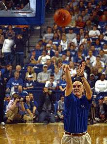 A man, wearing a blue shirt and brown pants, is shooting a basketball on a basketball court.