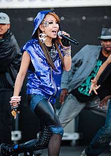 A young Korean female singing on stage wearing a sequined blue hoodie with blue and black tights.