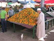 A stand with oranges, a man next to it, a cat on the floor