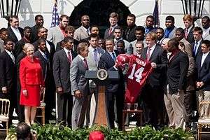 President Obama receives an Alabama jersey at the White House with various team members and coaches present.