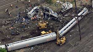 Aerial view of two intact passenger cars resting on their side and one passenger car warped and split open