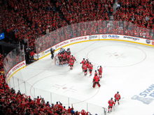 Several members of the team embrace in celebration as the crowd around the ice surface cheers.