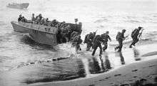 black & white photograph of Marines disembarking a landing craft at a beachhead