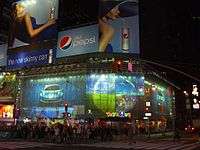 Outside of large, brightly lit store at night in New York City, surrounded by advertisements