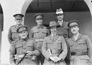 Six senior Australian officers pose for a formal picture. Two are wearing slouch hats, the remainder are wearing peaked caps. All have multiple ribbons.