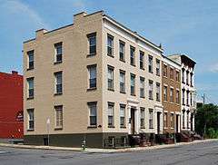 A group of four attached three-story brick buildings with flat roofs and stoops. The two closest to the camera are tan, the third brown and the last white.