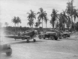 Single-engined military aircraft parked on tropical field beside petrol trucks