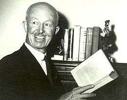 Head-and-shoulders informal portrait of bald man with moustache, holding an open book