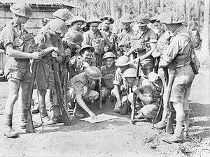 Soldiers in tropical uniforms stand around a map prior to a patrol