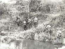 Soldiers slowly advance up a hill along the side of a waterway