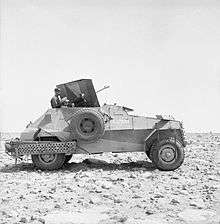 A four-wheeled armoured car, faces to the right, on a stony-desert backdrop.