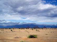 Desert under mostly cloudy sky, with hills in background