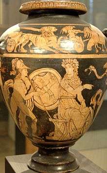 An image painted on the body of a vase. A seated woman speaks to a man behind her while her hand gestures forward. The man wears greaves and a helmet and holds a shield and a spear.