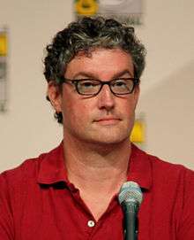 A man with glasses and a red shirt is sitting in front of a microphone.