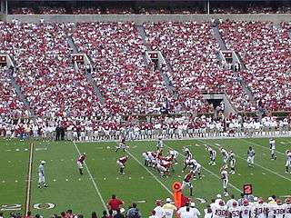 Alabama lines up on offense with Arkansas on defense on an American football field with a large crown in the stands.