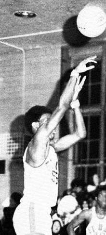 A man, wearing a white jersey, is shooting a basketball.
