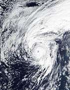 A well-developed hurricane with a defined, clear eye and prominent clouds surrounding it. A large band of clouds also extends north of the main center