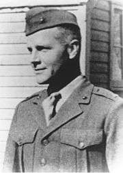 Head and shoulders of a young white man wearing a garrison cap and a plain military jacket over a shirt and tie