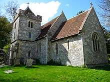 A short flint church with a red tiled roof, and a battlemented south tower with a pyramidal roof