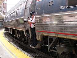 An Amtrak conductor standing in the doorway of an Amfleet cars with its trapdoor in the open position