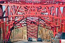 A red steel bridge arch seen from a car going under the metalwork along the bridge deck