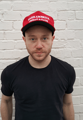 Photographc portrait of a young man, wearing a black T-shirt and a red baseball cap with Donald Trump's "Make America Great Again" slogan