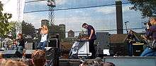 Annie, a drummer, and a keyboardist performing to a crowd at an outdoor festival.