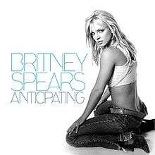 Image of a blond woman. She sits on the right side of the image. She wears low-cut jeans, boots and a white top. She is looking over her shoulder into the camera. On the left, the words "BRITNEY SPEARS ANTICIPATING" are written in big blue capital letters.