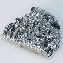 A glistening silver rock-like chunk, with a blue tint, and roughly parallel furrows.
