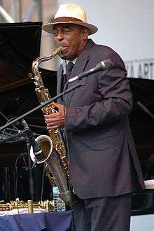 Archie Shepp on stage in a suit playing saxophone