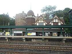 A view of an ornate structure with railroad tracks and a modern elevated platform and metallic structure in the foreground