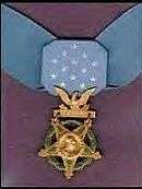 A light blue neck ribbon with a gold star shaped medallion hanging from it. The ribbon is similar in shape to a bowtie with 13 white stars in the center of the ribbon.