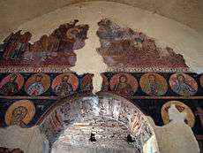 A partially preserved fresco of a biblical scene with portraits of Christian figures in circles below, all painted above a portal