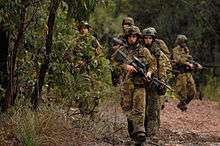 A group of Australian soldiers with rifles moving along a path in a wooded area