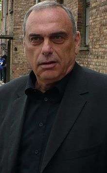The head and upper torso of an Israeli gentleman in his 50s. He has short grey hair and is wearing a black shirt with the top button undone, and a dark grey jacket.