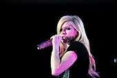 Avril Lavigne wearing a black gown and sining in to a microphone.