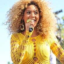 A picture of a blonde woman wearing a yellow outfit performing.