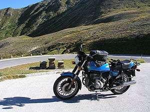 Blue BMW R65 motorcycle with tank bag, parked close to a bend in a mountain road