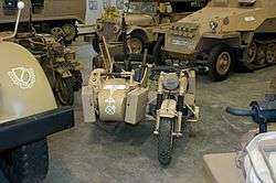 Located in a museum among other vehicles, a front view of a desert camouflage BMW R75 motorcycle and sidecar